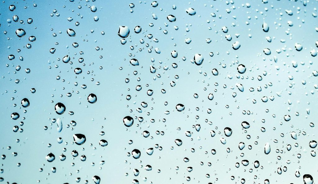 Close-up view of water droplets on glass against a blue sky background.